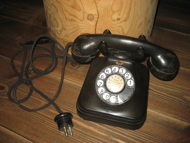 Gammel telefon med tallskive og tekst: BRUK SKIVEN NÅR SUMMETONEN HØRES. 40-50 tallet.