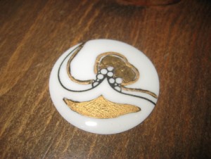 Jakkenål i dekorert porselen, ca 4.5 cm i diameter. Nål er ikkje festa på baksida, dette er en smal sak. 