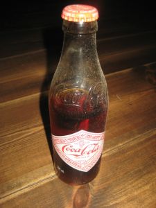 Uåpna Coca Cola flaske fra 1986. Noe av innholdet er dampa bort. Engelsk??  20 cm høg.